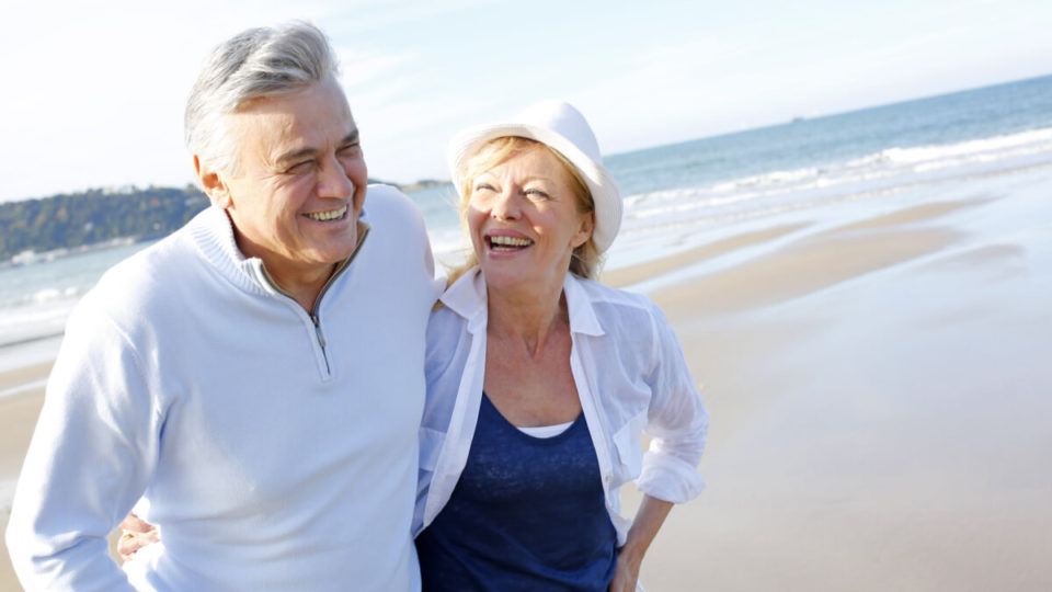 Older couple laughing, walking on beach