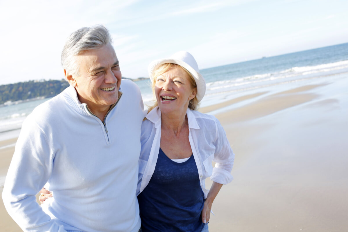 Older couple laughing, walking on beach